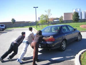 Three young people pushing a brokedown car