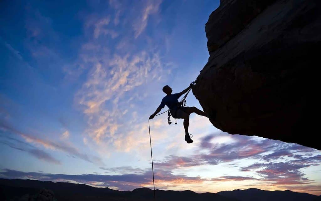 Mountain Climber Holding on by one hand over a vertical drop